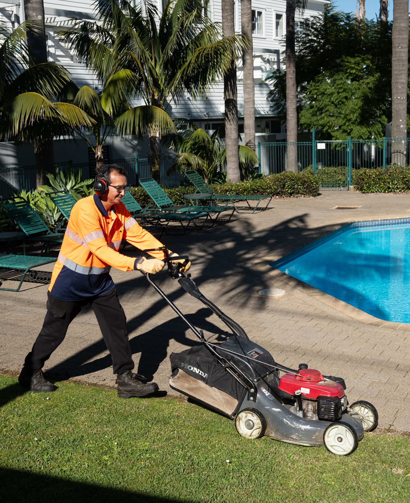 Masterscape crew member operating a Honda lawn mower beside a swimming pool at a residential body corporate complex in Auckland