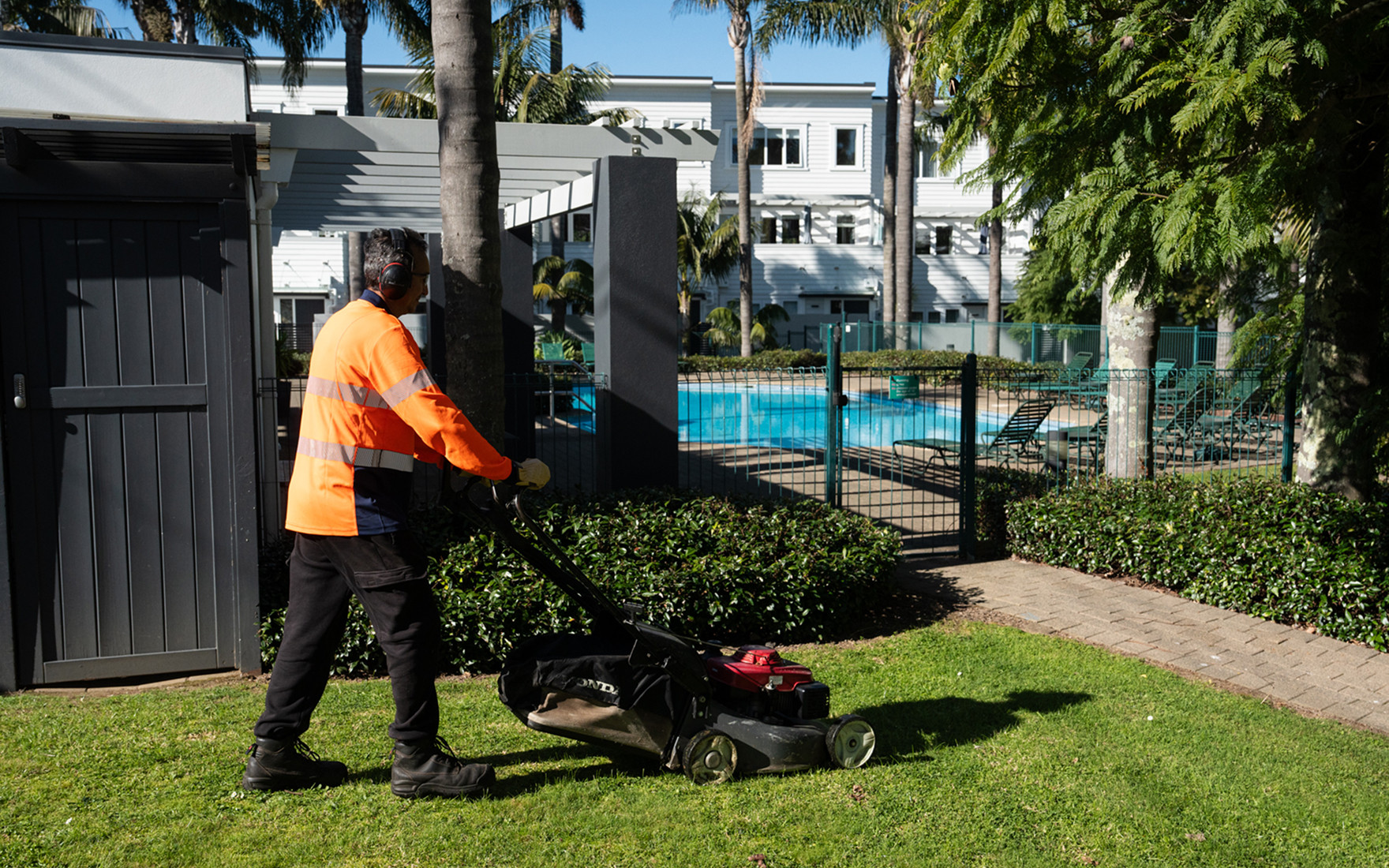 Masterscape crew member mowing lawns in a well-maintained garden area at a body corporate complex with pool in Auckland