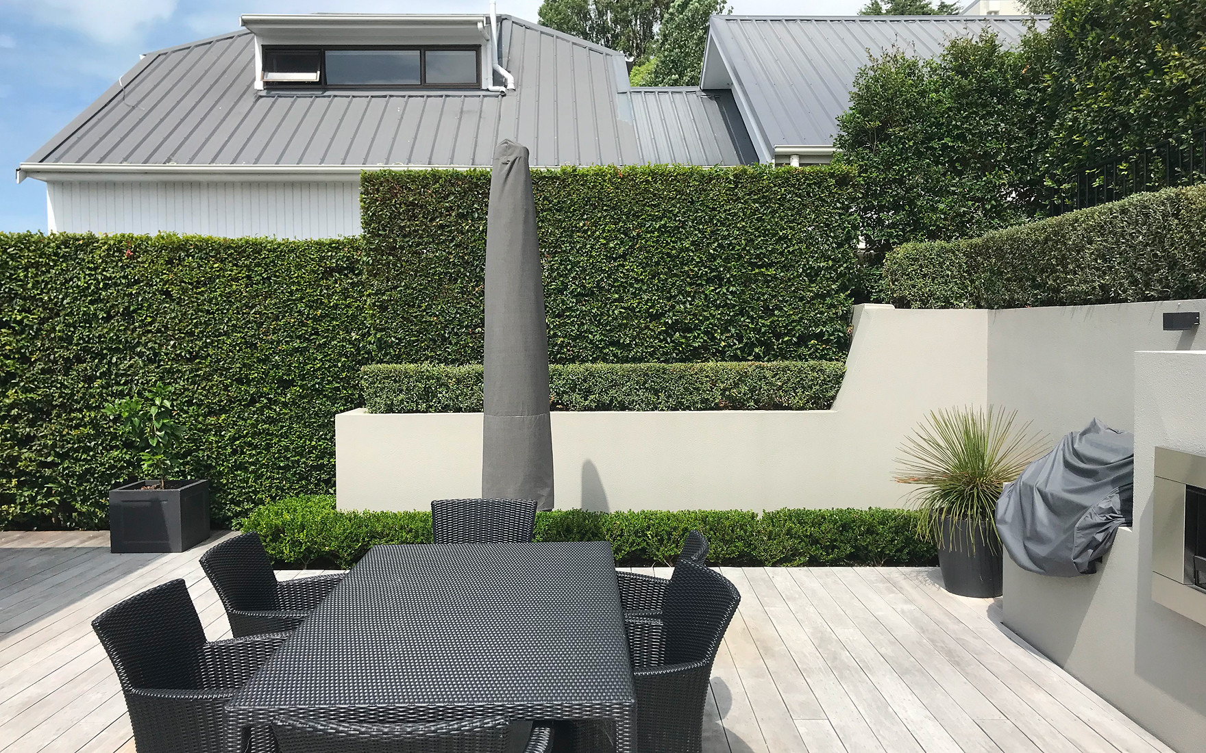 Immaculately trimmed hedges and manicured garden beds surrounding a luxury outdoor entertaining area in Auckland, maintained by Masterscape