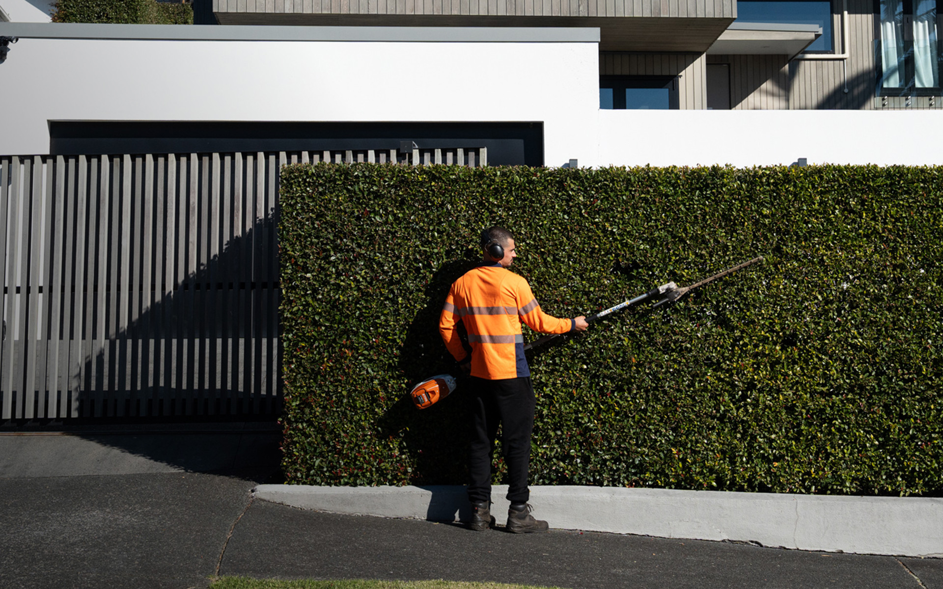 Masterscape crew member trimming a tall formal hedge at a high-end residential property in Auckland